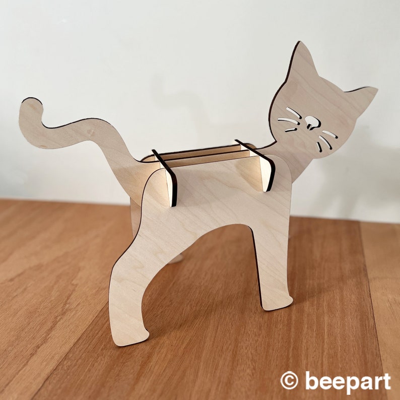 May include: A wooden cat-shaped organiser with a shelf for holding items. The cat is made of light wood and has a black outline.