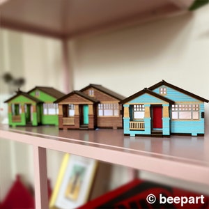 May include: Four miniature wooden houses in different colors, including blue, green, brown, and beige, are arranged on a shelf. The houses have small windows and doors, and some have porches.