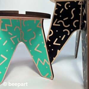 May include: Two wooden stools with geometric patterns. One stool is painted black with white geometric patterns, and the other is painted teal with white geometric patterns.