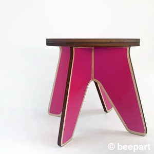 K&ouml;nnte beinhalten: Ein rosa-brauner Holzhocker mit einem einzigartigen A-Rahmen-Design. Der Hocker hat eine glatte, gl&auml;nzende Oberfl&auml;che und ist perfekt, um jedem Raum einen Farbtupfer zu verleihen.