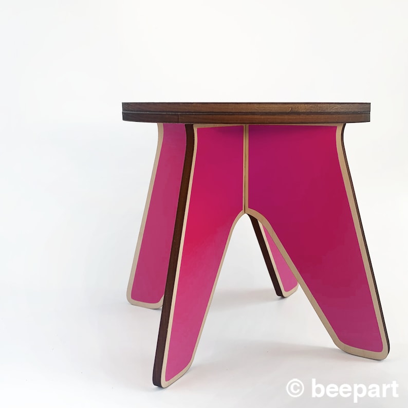 K&ouml;nnte beinhalten: Ein rosa-brauner Holzhocker mit einem einzigartigen A-Rahmen-Design. Der Hocker hat eine glatte, gl&auml;nzende Oberfl&auml;che und ist perfekt, um jedem Raum einen Farbtupfer zu verleihen.
