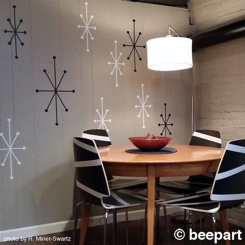 Puede incluir: Un comedor con una mesa redonda de madera y cuatro sillas rayadas en blanco y negro. Las paredes est&aacute;n pintadas de gris claro y decoradas con calcoman&iacute;as de estrellas negras y blancas. Una l&aacute;mpara blanca con un brazo curvo cuelga sobre la mesa.