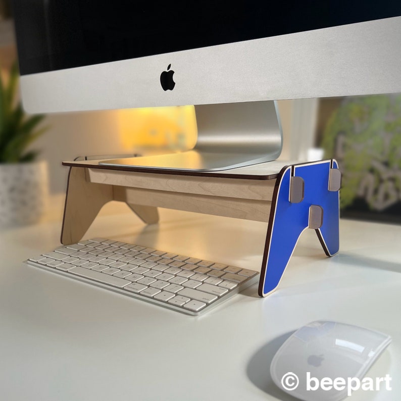 May include: A wooden computer monitor stand with a blue, gamer-style design. The stand is raising a computer monitor above a white keyboard and a white mouse.