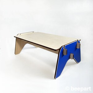 May include: A wooden table with a blue, game controller-shaped base. The table top is made of light wood and has a brown border.