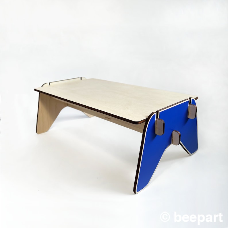 May include: A wooden table with a blue, game controller-shaped base. The table top is made of light wood and has a brown border.