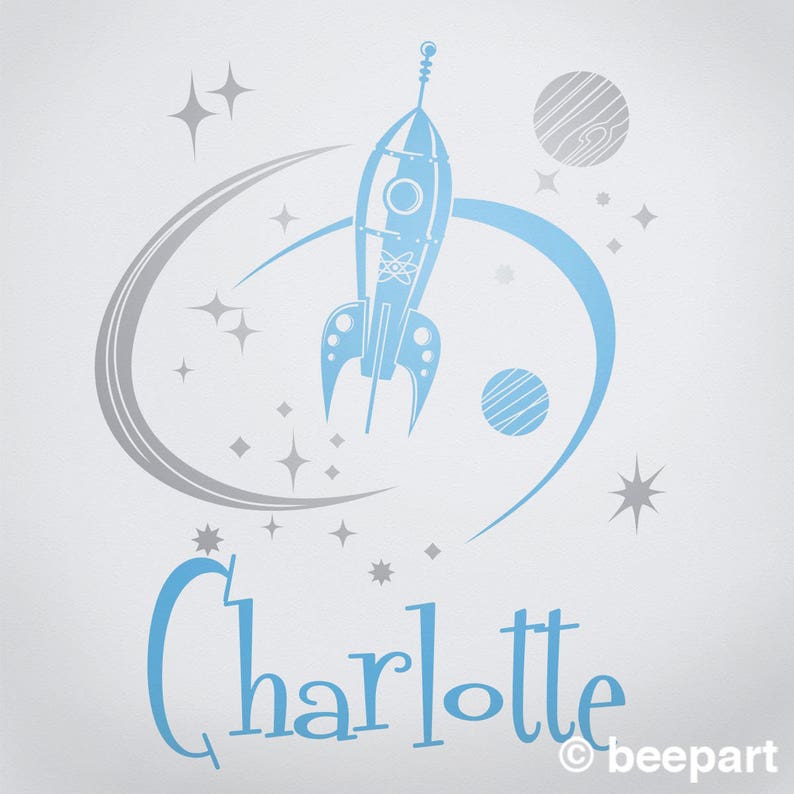 May include: A blue rocket ship with a silver atom symbol on the side, flying through a silver orbit with two silver planets and stars. The name Charlotte is written in blue below the rocket.