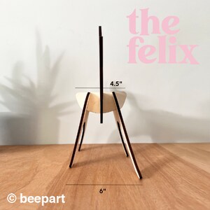 May include: A wooden chair stand with black accents. The stand is 6 inches wide and 4.5 inches tall. The stand is made of plywood and has a simple design.