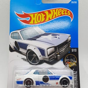 May include: A white Nissan Skyline H/T 2000GT-X Hot Wheels die-cast car with blue and black accents. The car is part of the Nightburnerz series and is number 9 of 10 in the series. The car is on a blue and white card with the Hot Wheels logo.
