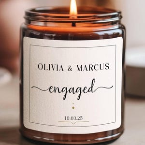 Puede incluir: Una vela de vidrio marrón con una etiqueta blanca que dice "Olivia & Marcus comprometidos 10.03.25".