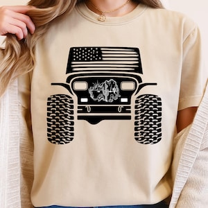 Peut inclure: T-shirt beige avec un motif noir d'une Jeep avec un drapeau américain en haut. La Jeep a de gros pneus et une scène de désert au centre.