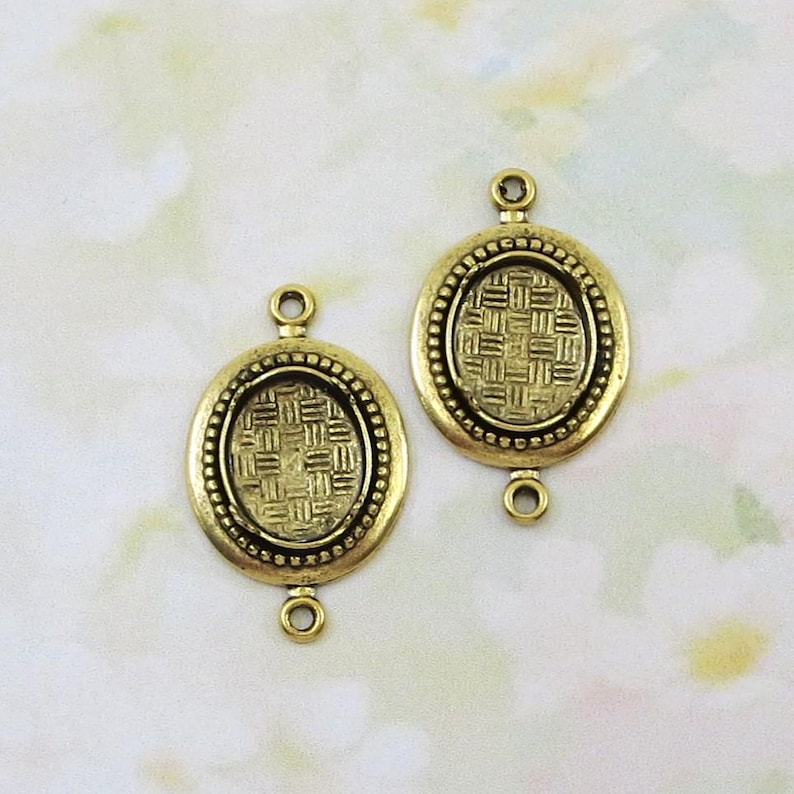 May include: Two antique gold-colored oval jewelry connectors. Each connector features a woven pattern within an oval frame, surrounded by a beaded border. They have loops at the top and bottom for attaching to other jewelry components.
