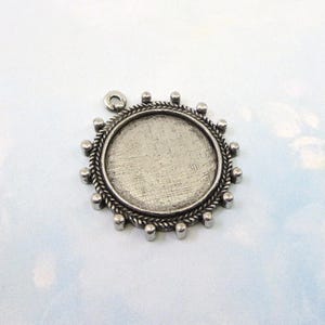 May include: Silver pendant with a round, textured, metal frame and a loop at the top. The frame has a beaded edge.