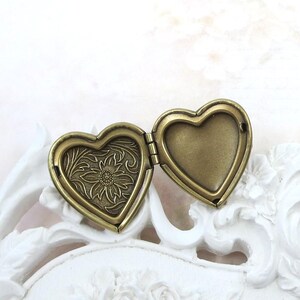 May include: An open heart-shaped locket made of antique brass-toned metal. The left interior panel features an embossed floral pattern with a central flower, while the right interior panel is smooth and plain, designed for holding a small photograph.