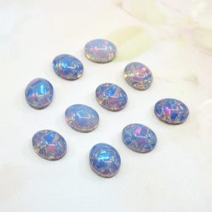 Può includere: Dieci cabochon ovali iridescenti con un motivo a mosaico. I cabochon presentano una miscela di tonalità blu, rosa e viola. Sono disposti su una superficie bianca, adatti per la creazione di gioielli o progetti artigianali.