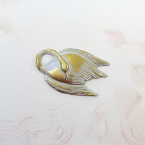 Könnte beinhalten: Ein goldener und weißer Schwanen-Anhänger mit detailliertem Design. Der Schwan befindet sich in Flugposition mit ausgebreiteten Flügeln.