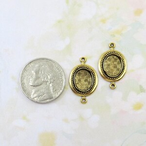 May include: Two antique gold-colored oval connector charms with a woven pattern in the center and a beaded border. Each charm has a loop at the top and bottom for attaching to other jewelry components. A nickel coin is next to the charms.
