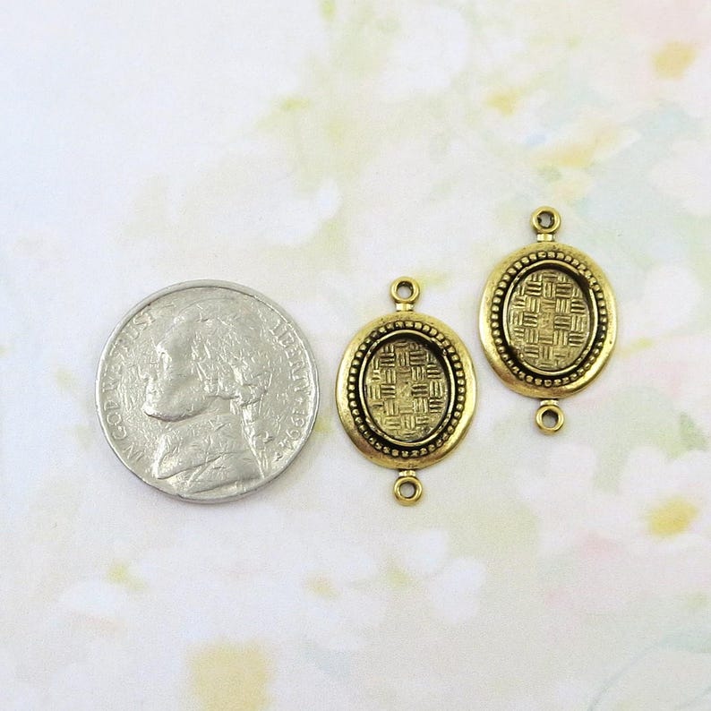 May include: Two antique gold-colored oval connector charms with a woven pattern in the center and a beaded border. Each charm has a loop at the top and bottom for attaching to other jewelry components. A nickel coin is next to the charms.