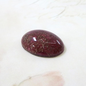 May include: A deep burgundy oval cabochon with gold glitter embedded in the resin. The cabochon has a smooth, glossy finish.