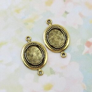 May include: Two antique gold-colored oval connector charms. Each charm features a woven pattern within an oval frame, surrounded by a beaded border. The charms have loops at the top and bottom for attaching to other jewelry components.