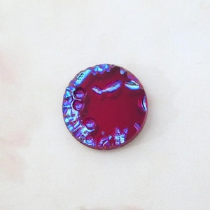 May include: A round, iridescent glass cabochon with a deep red color and a textured, bubbly surface. The cabochon has a blue and purple iridescent sheen.