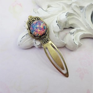 May include: A vintage-style brass bookmark with an oval, multi-colored opal-like stone. The stone features shades of blue, pink, and orange. The bookmark has an ornate design around the stone and a simple, elongated body.