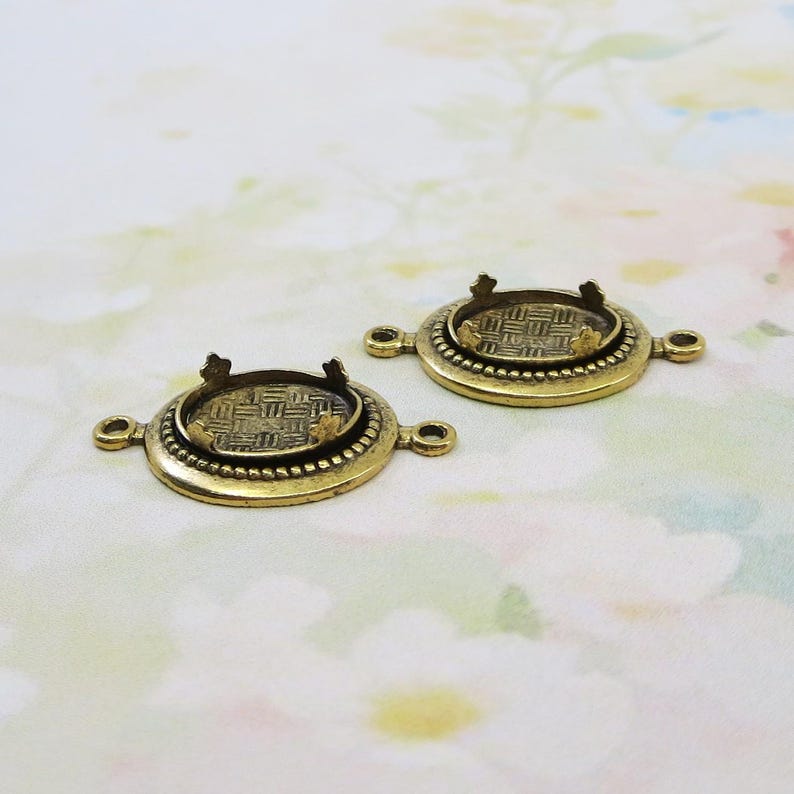 May include: Two antique brass-colored jewelry findings. Each finding has a round, textured bezel setting with four prongs and a decorative beaded edge. The findings also have loops on either side for attaching to other components.