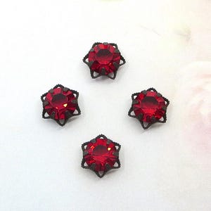 May include: Four circular red faceted gemstones set in dark metal filigree prong settings. Each stone is round and features a vibrant crimson hue, held securely by a decorative, scalloped metal frame that creates a star-like outline around the gem.