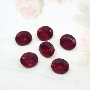 May include: Five oval-shaped, deep red faceted gemstones arranged in a cluster. Each stone features a polished surface with multiple geometric cuts that reflect light, creating a brilliant appearance across the dark crimson surfaces of the gems.
