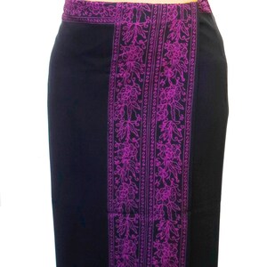 Solid black sarong with a purple floral border on all four edges. Shown as a straight skirt with the purple floral border at the waist, flowing down the front and lining the bottom at the ankles.