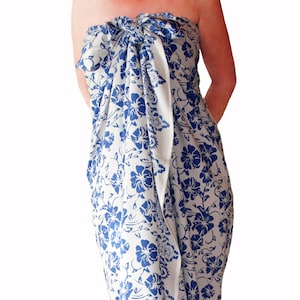 White sarong with blue hibiscus flower. It is tied as a dress with a knot breast level and covers to just below the knees.