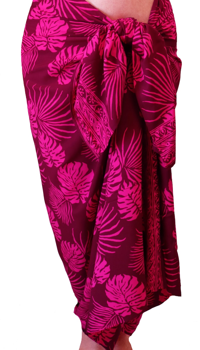 Maroon sarong with large hot pink jungle leaves. It is tied in a knot at the hips and covers to the feet, worn as a full-length skirt or beach cover up.