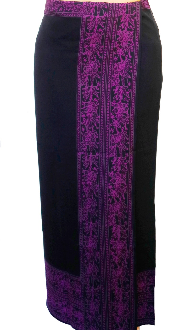 Solid black sarong with a purple floral border on all four edges. Shown as a straight skirt with the purple floral border at the waist, flowing down the front and lining the bottom at the ankles.