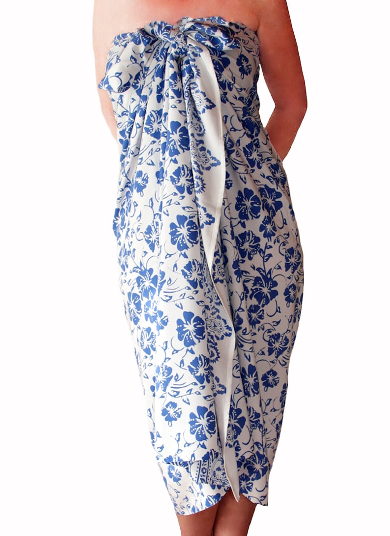 White sarong with blue hibiscus flower. It is tied as a dress with a knot breast level and covers to just below the knees.