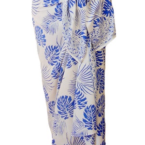 White sarong with large blue jungle leaves. It is tied in a knot at the hips and covers to the feet, worn as a full-length skirt