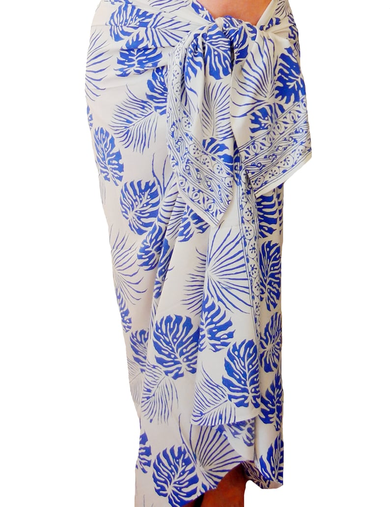 White sarong with large blue jungle leaves. It is tied in a knot at the hips and covers to the feet, worn as a full-length skirt