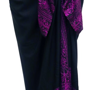Black sarong wrapped as a skirt and tied at the waist. It has a 6 inch purple floral border that goes all the way around on all four sides. The purple border wraps around the hips, drapes down the front and lines the bottom at the ankles.