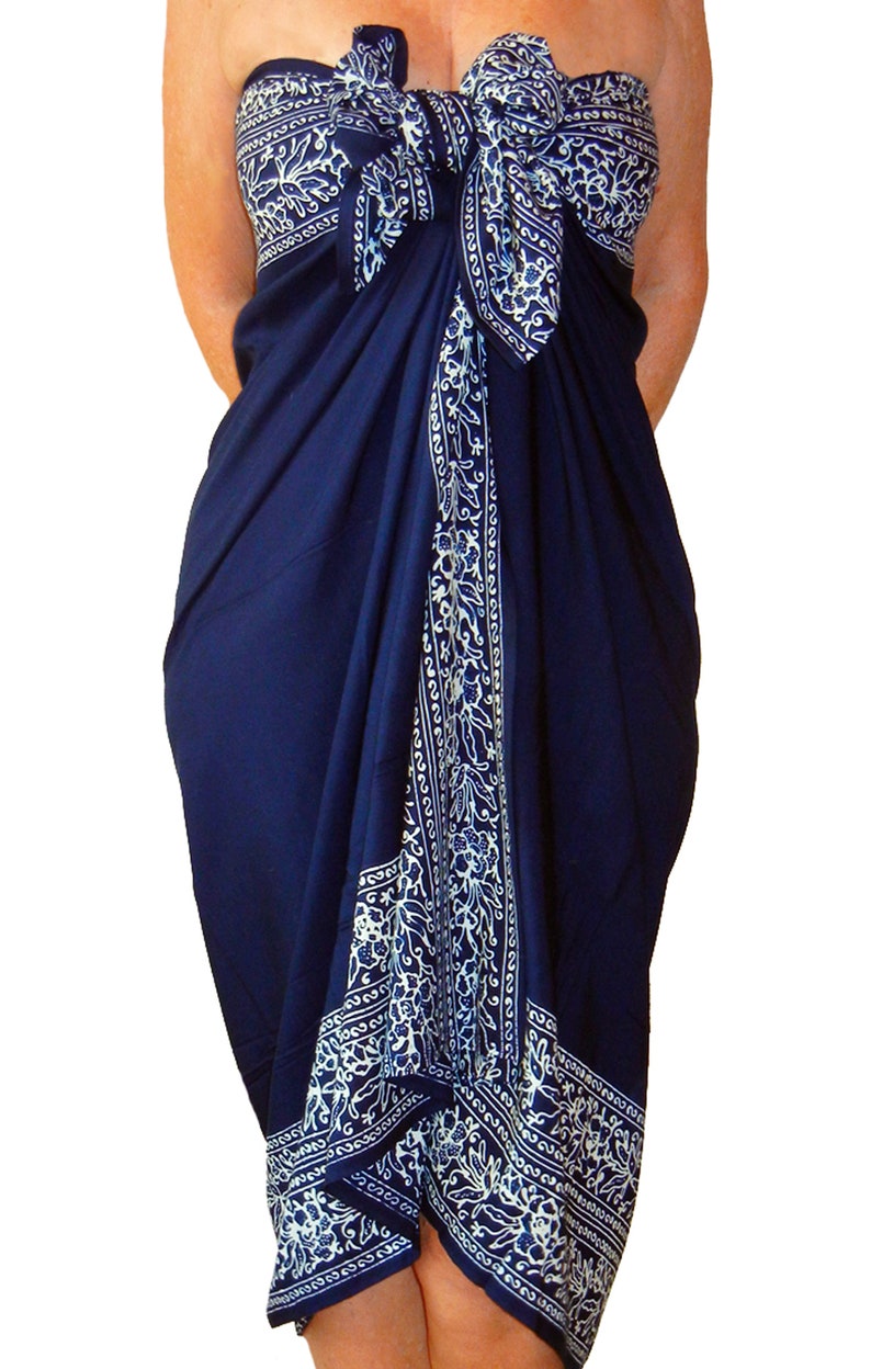Navy blue sarong with a  white floral border that goes all the way around on all four sides. It is tied as a dress with a bow at the breast line. The border design flows down the front, across the breast line, and hems the bottom at the knee.
