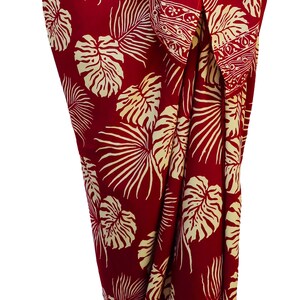 Red sarong with large jungle leaves in creamy white. It is tied in a knot at the hips and covers to the feet, worn as a full-length skirt.