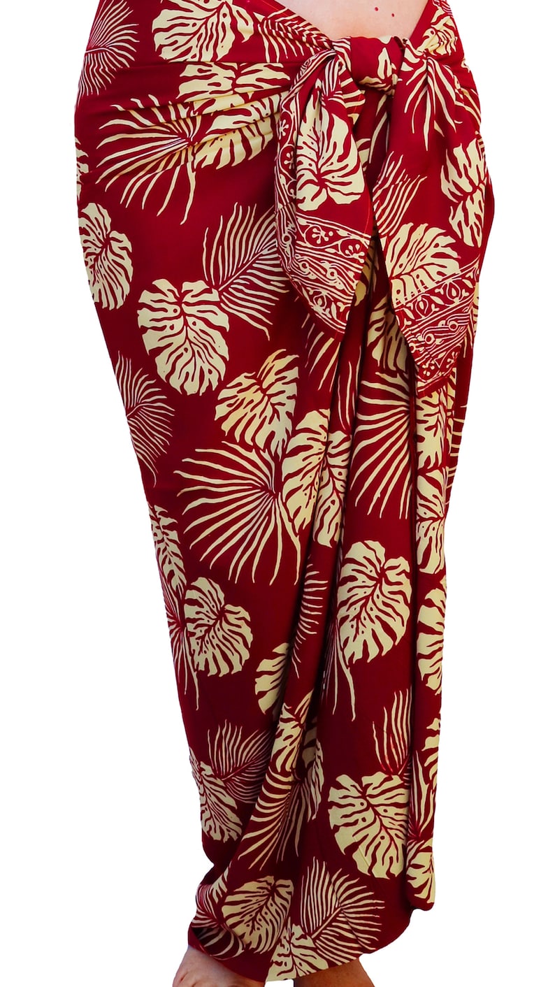 Red sarong with large jungle leaves in creamy white. It is tied in a knot at the hips and covers to the feet, worn as a full-length skirt.