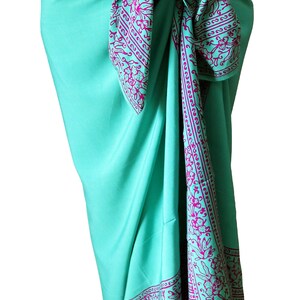 Teal green sarong wrapped as a skirt and tied at the waist. It has a 6 inch purple floral border that goes all the way around on all four sides. The purple border wraps around the hips, drapes down the front and lines the bottom at the ankles.