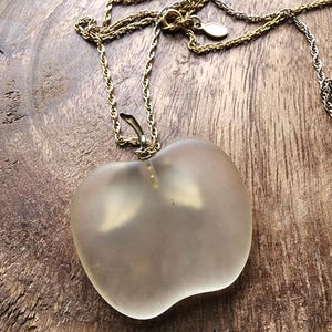 May include: A gold-toned necklace with a frosted glass apple pendant. The apple pendant is a light, translucent color and has a stem detail. The necklace chain is delicate and has a lobster clasp.