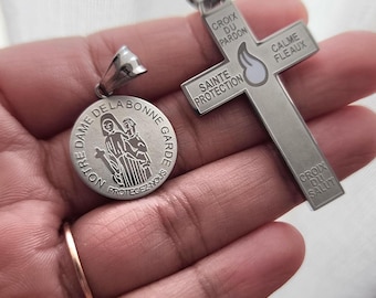 May include: A silver-toned circular pendant featuring an engraving of Notre Dame de la Bonne Garde and a silver-toned cross pendant inscribed with Croix du Pardon, Calme Fleaux, Sainte Protection, and Croix du Salut with a central flame icon.