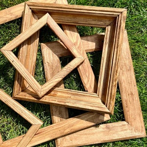 Puede incluir: Cuatro marcos de fotos de madera de diferentes tamaños, apilados uno encima del otro, sobre una superficie de hierba verde.