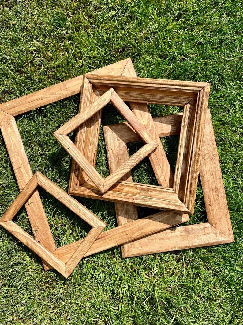 May include: Four wooden picture frames of varying sizes, stacked on top of each other, on a green grassy surface.
