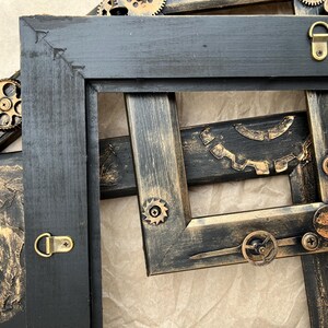 May include: Two black picture frames with gold accents and steampunk-inspired metal gears and cogs. The frames are distressed and have a vintage look.