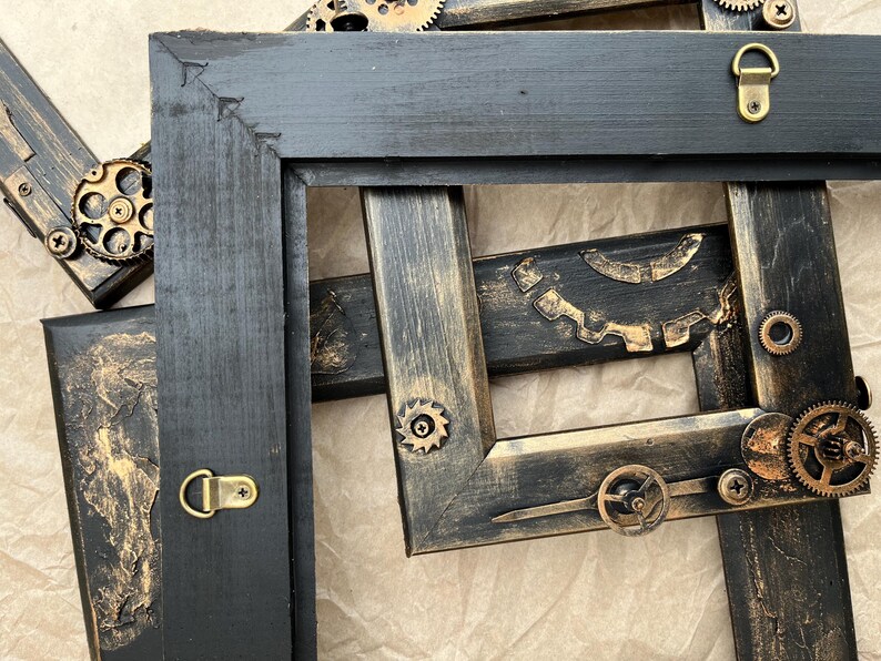 May include: Two black picture frames with gold accents and steampunk-inspired metal gears and cogs. The frames are distressed and have a vintage look.