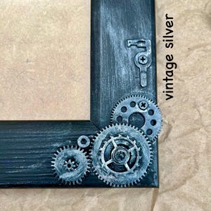 May include: A black picture frame with a distressed finish and silver gears and a keyhole design. The frame has the text "vintage silver" written on it.