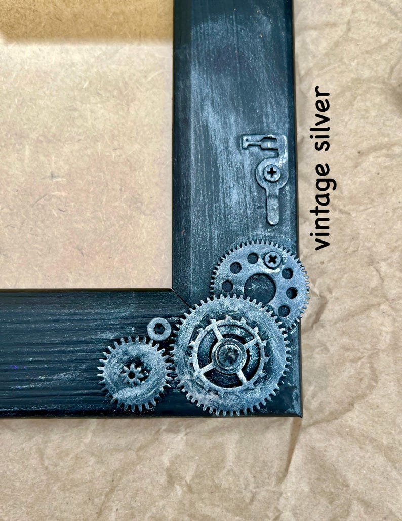 May include: A black picture frame with a distressed finish and silver gears and a keyhole design. The frame has the text "vintage silver" written on it.