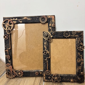 May include: Two black picture frames with a steampunk design. The frames are decorated with gears, pipes, and other industrial elements. The frames are made of wood and have a distressed finish.
