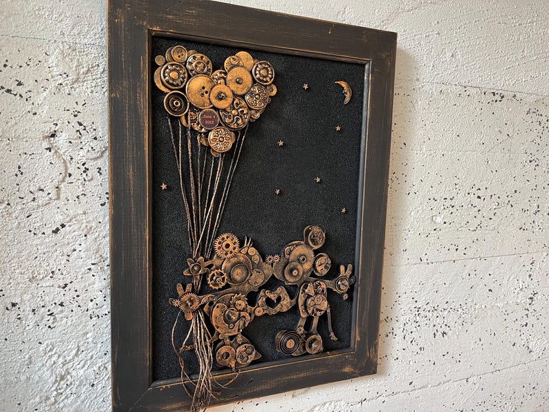 May include: A framed artwork featuring a heart-shaped balloon made of buttons and gears, with a pair of Mickey Mouse characters made of gears and metal pieces below. The background is black with white stars and a crescent moon.
